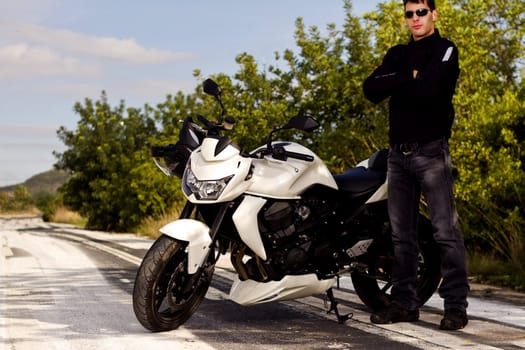 View of a man with a motorcycle on a asphalt road.
