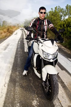 View of a man with a motorcycle on a asphalt road.
