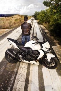 View of a man with a motorcycle on a asphalt road.