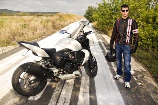 View of a man with a motorcycle on a asphalt road.