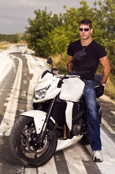 View of a man with a motorcycle on a asphalt road.
