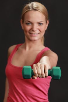 Young blonde woman doing exercise with dumbbells isolated against a black background.Selective focus on the dumbbells