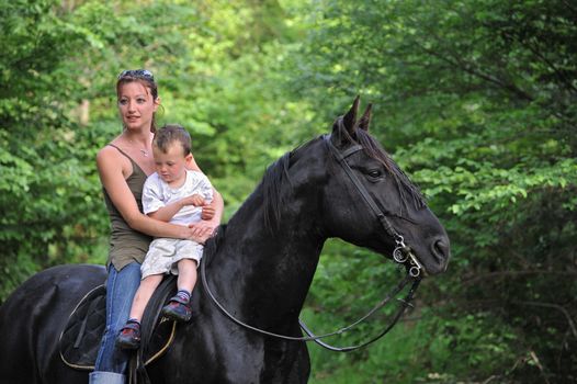 young woman, little boy and their black stallion in a forest