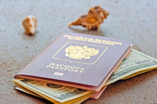 Russian passport with a dollar invested and seashells on a granite table top