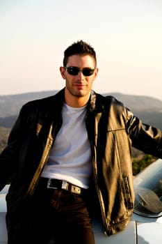 View of a young male with a jacket next to his white convertible car.