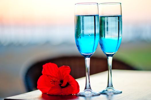 Two glasses with blue alcohol cocktail with an exotic flower on the table