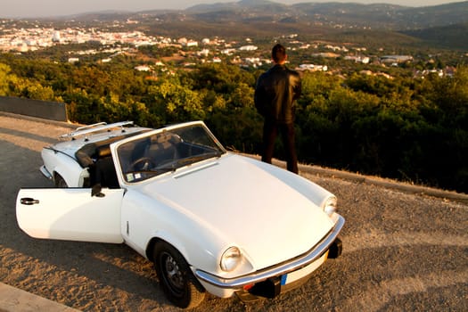 View of a young male with a jacket next to his white convertible car.