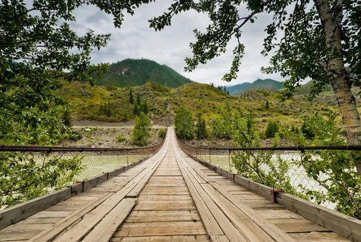 Wooden suspension road bridge on the river Katun. Altai Mountains, Russia.