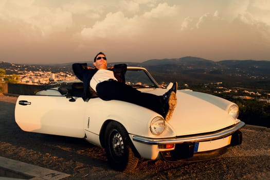 View of a young male with a jacket next to his white convertible car.