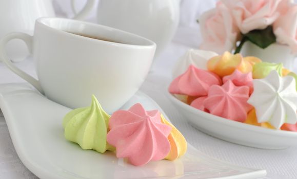 Meringue cookies of different colors on a plate with a cup of coffee close up