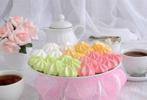 Meringue cookies of different colors on a plate with a cup of coffee