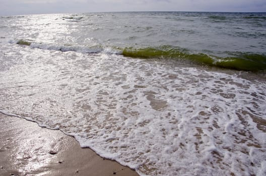 Sea waves beating shore sand and sun reflection on water.