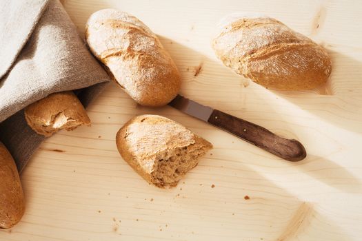 broken rye bun with rye buns and a knife from top on wooden background