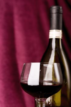 red wine in glass and bottle on a claret background