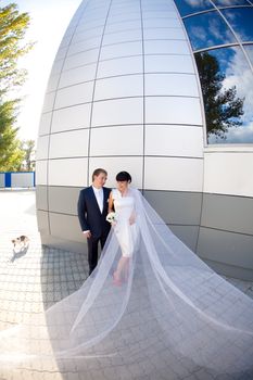 bride and groom by the wall with long flying veil