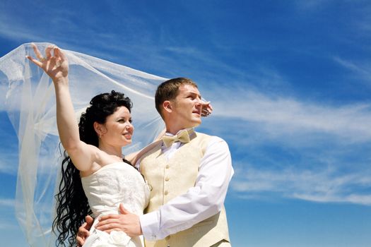 bride and groom under the veil on the blue sky