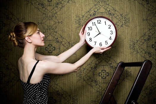 An image of a young woman hanging a clock on the wall