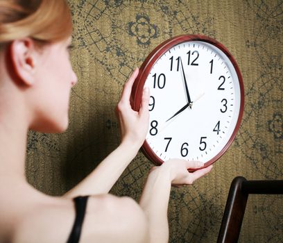 An image of a young woman hanging a clock on the wall