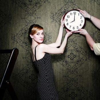 An image of a woman hanging  a clock on the wall