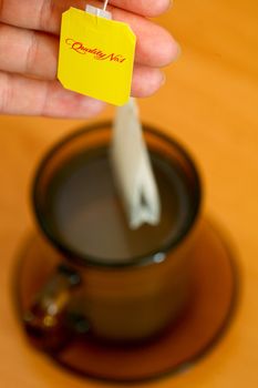 Womans hand holding tea bag on background of cup of tea