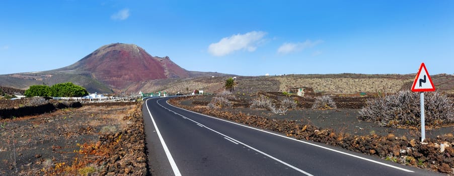 Empty road crossing the lava in the mountain, volcano backround. Panorama. Lanzarote, Canary islands, Spain