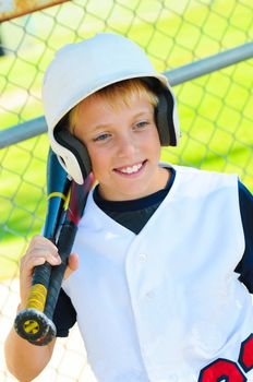Cute baseball player smiling in the dugout about to go bat.
