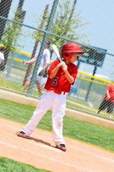 Little league baseball player in red jersey waiting to bat using a wood bat.