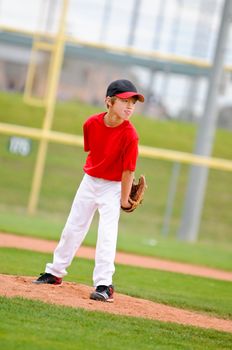 Little league baseball pitcher on the mound wearing a red jersey.