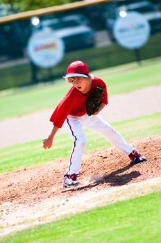 Youth baseball pitcher after pitch wearing a red jersey.