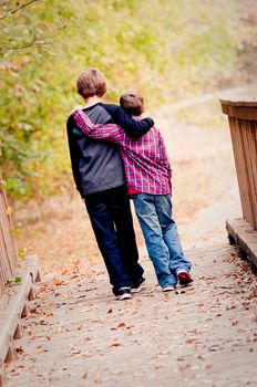 Two brothers with arms around each other walking on a bridge outdoors.