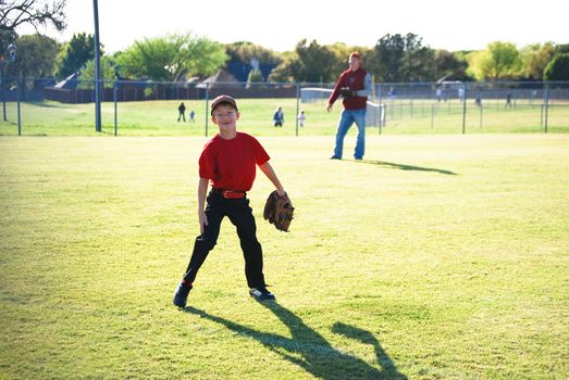 Little league baseball player laughing in outfield looking at camera.