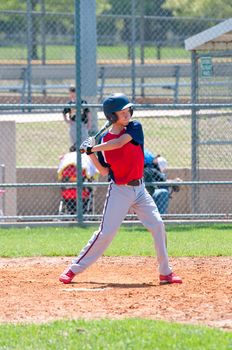 Teen boy baseball player swinging bat.