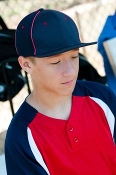 Teen baseball player looking sad in dugout.