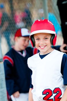 Little league baseball boy with helmet in dugout smiling.