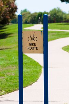 Posted blue and yellow rusty bike route sign near a path.