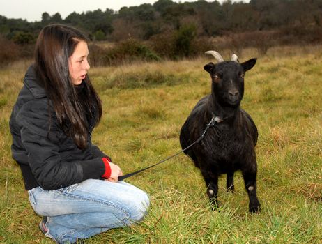 young teenager and a black miniature goat in a field