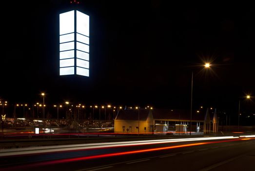 Night photo of empty billboard in the shopping park. Blurred lights of cars in the foreground.