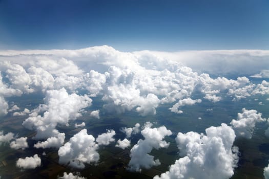blue sky and clouds and fields visible through them from a plane window