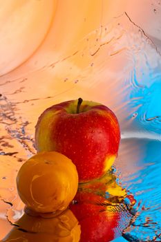 ripe red apple and yellow plum over pink and blue background