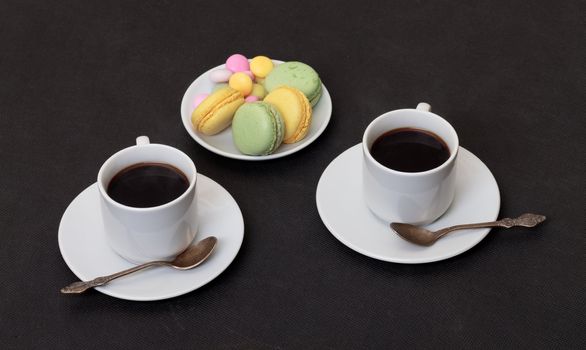 Two cups coffee and macaroon, on black