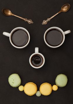 Tree cups coffee and macaroon arranged in happy face, on black