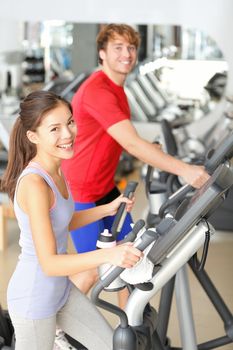 Gym people in fitness center doing walking workout on moonwalker fitness machines. Young couple, asian girl and caucasian man training in gym smiling happy.