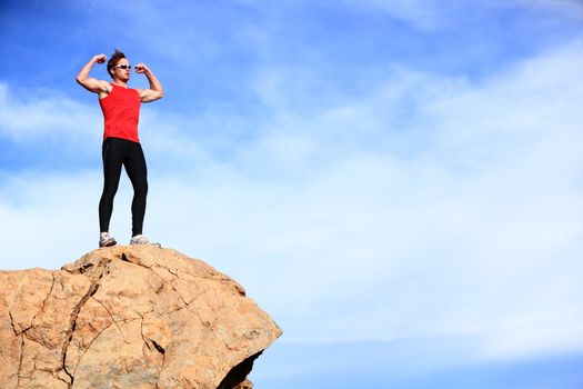 Success - winner man on mountain top celebrating showing muscles in sporty outfit. Fit caucasian male fitness model cheering on top of the world.