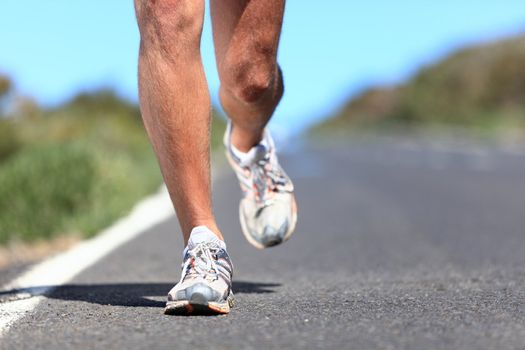 Running shoes - runner legs and running shoe closeup of man jogging outdoors on road.