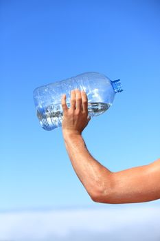 Thirsty man drinking water of big bottle. Closeup of hand holding bottle. Thirst concept image from outdoors on blue sky above the clouds.