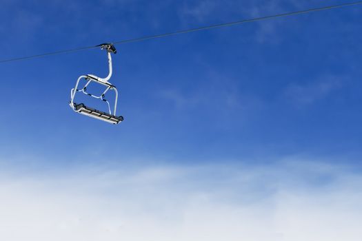 Empty ski lift chair for four persons elevating on bright blue sky background
