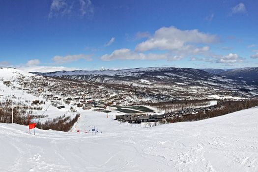 Panoramic view of ski route, village and sky  taken from slope in bright winter day