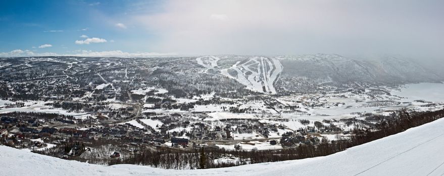 Panoramic view of small city in the valley with winter mountain slopes taken from the ski route