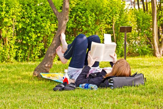 Young girl with a book lying on a lawn in a park
