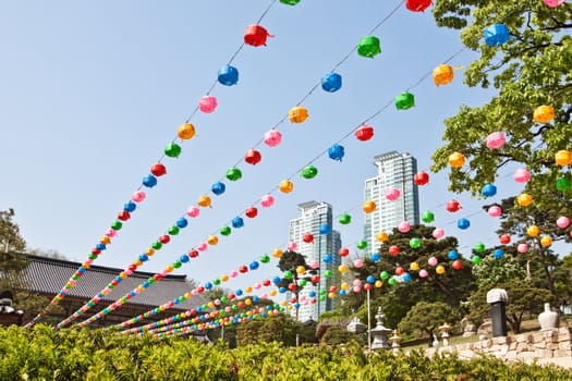 Colorful lanterns hanging near buddhist temple with sky and skyscrapers at background